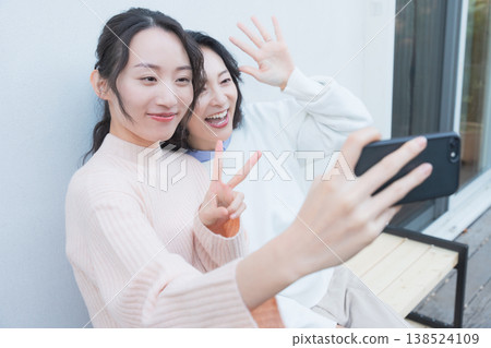 A portrait of a close mother and daughter taking a selfie with their smartphone on a retro-style veranda. A portrait of a close mother and daughter taking a selfie with their smartphone on a retro-style veranda. 138524109