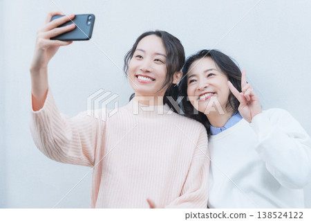 A portrait of a close mother and daughter taking a selfie with their smartphone on a retro-style veranda. A portrait of a close mother and daughter taking a selfie with their smartphone on a retro-style veranda. 138524122
