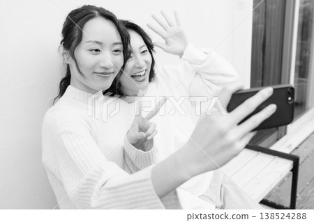 A monochrome portrait of a close mother and daughter taking a selfie on the veranda with their smartphones. A monochrome portrait of a close mother and daughter taking a selfie on the veranda with their smartphones. 138524288