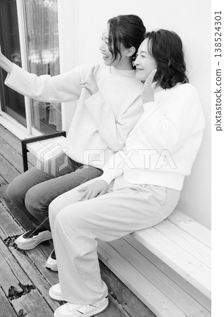 A monochrome portrait of a close mother and daughter taking a selfie on the veranda with their smartphones. 138524301