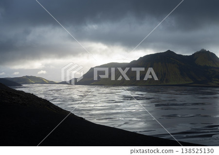 Sun setting behind mountains in glacial landscape with heavy storm clouds above, Iceland Sun setting behind mountains in glacial landscape with heavy storm clouds above, Iceland 138525130