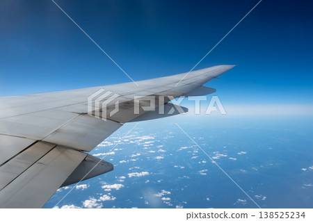Airplane wing cutting across a vast blue sky dotted with fluffy clouds, conveying flight, travel and freedom from a high altitude window perspective over the horizon Airplane wing cutting across a vast blue sky dotted with fluffy clouds, conveying flight, travel and freedom from a high altitude window perspective over the horizon 138525234