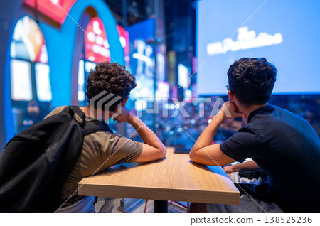 Times square, new york, usa august 14,2024. Male friends sitting at a table in a cafe, observing the vibrant night scene and bright led screens of times square Times square, new york, usa august 14,2024. Male friends sitting at a table in a cafe, observing the vibrant night scene and bright led screens of times square 138525236