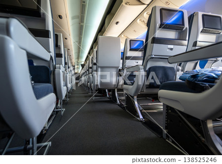 Empty airplane cabin aisle with rows of blue and white passenger seats featuring personal entertainment screens, illustrating modern air travel and journey preparation Empty airplane cabin aisle with rows of blue and white passenger seats featuring personal entertainment screens, illustrating modern air travel and journey preparation 138525246
