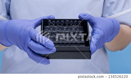 Dentist hands in blue gloves holding a box of transparent dental matrices or clear teeth samples. Dentist hands in blue gloves holding a box of transparent dental matrices or clear teeth samples. 138526220