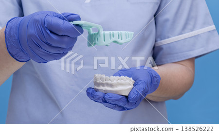 Dentist in blue gloves holding a dental impression tray and a plaster model of teeth. 138526222