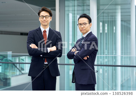 兩名日本商人站在辦公室裡,雙手交叉放在胸前,表情自信。 兩名日本商人站在辦公室裡,雙手交叉放在胸前,表情自信。 138526398