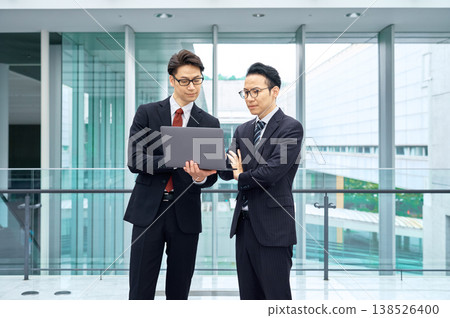 Two Japanese businessmen are having a meeting in an office building, looking at their laptops. Two Japanese businessmen are having a meeting in an office building, looking at their laptops. 138526400