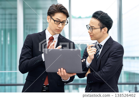 兩名日本商人正在辦公大樓開會,他們各自看著筆記型電腦。 兩名日本商人正在辦公大樓開會,他們各自看著筆記型電腦。 138526402
