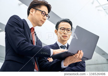 Two Japanese businessmen are having a serious discussion while looking at their laptops. Two Japanese businessmen are having a serious discussion while looking at their laptops. 138526406