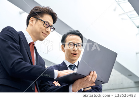 Two Japanese businessmen are having a meeting in their office, looking at their computers. Two Japanese businessmen are having a meeting in their office, looking at their computers. 138526488