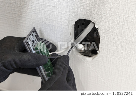 An electrician's hands as they install or replace electrical outlets and switches on a wall. An image depicting wiring work and renovations. An electrician's hands as they install or replace electrical outlets and switches on a wall. An image depicting wiring work and renovations. 138527241