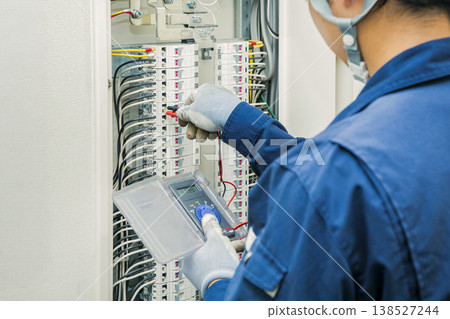 Electrician inspecting distribution boards and measuring voltage: Work scene. Building maintenance and inspection image. 138527244