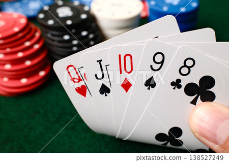 Hand holding Straight combination poker playing cards with colorful casino chips on green felt table gambling Hand holding Straight combination poker playing cards with colorful casino chips on green felt table gambling 138527249