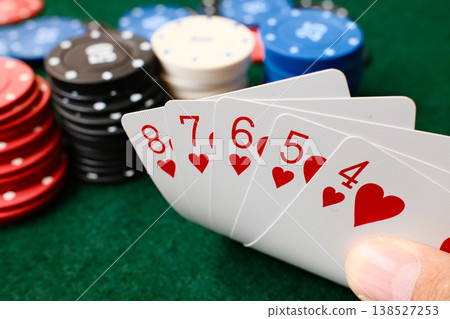 Hand holding Straight Flush combination poker playing cards with colorful casino chips on green felt table gambling Hand holding Straight Flush combination poker playing cards with colorful casino chips on green felt table gambling 138527253
