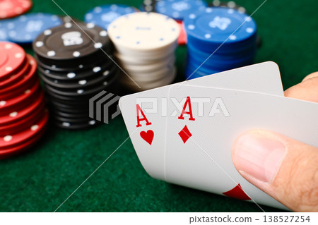 Hand holding a pair of aces poker playing cards with colorful casino chips on green felt table gambling Hand holding a pair of aces poker playing cards with colorful casino chips on green felt table gambling 138527254