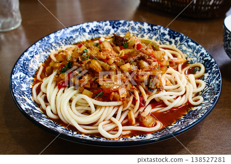 Uyghur suiru lagman noodles with spicy meat tomato vegetable sauce in blue bowl on restaurant table setting Uyghur suiru lagman noodles with spicy meat tomato vegetable sauce in blue bowl on restaurant table setting 138527281