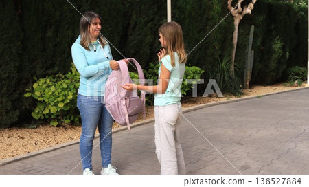 Caring mother in light blue hoodie listens attentively to her young daughter holding a pink backpack  138527884