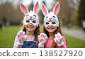 Two young girls wearing bunny masks and gloves, celebrating spring in a vibrant outdoor setting 138527920