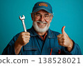 Smiling senior mechanic in uniform and cap, holding a wrench and giving thumbs up on blue background 138528021