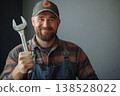 Smiling mechanic in cap and overall holding a large wrench, studio portrait on gray background 138528022