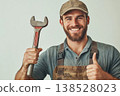 Smiling repairman in cap and overall holding wrench and showing thumbs up on light background 138528023