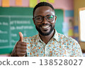 Smiling male teacher in glasses giving thumbs up in classroom, chalkboard and colorful notes in background 138528027