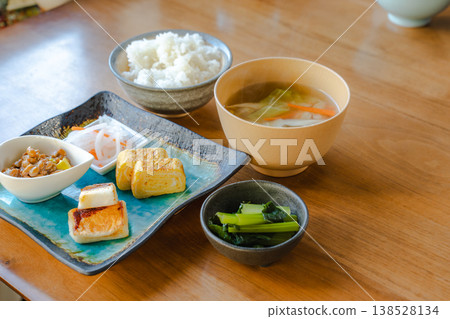A Japanese breakfast set featuring tamagoyaki (rolled omelet) and hanpen (fish cake) arranged on a wooden table. A Japanese breakfast set featuring tamagoyaki (rolled omelet) and hanpen (fish cake) arranged on a wooden table. 138528134