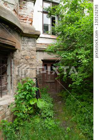 Overgrown Abandoned Stone House With Broken Windows And Rustic Wooden Door Amidst Lush Green Vegetation In Summer Overgrown Abandoned Stone House With Broken Windows And Rustic Wooden Door Amidst Lush Green Vegetation In Summer 138528298