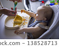 Child Refuses Spoon. Infant Playfully Defies Feeding. Baby Mockingly Challenges During Meal Time. Humorous Scene Where Young Child Resists Spoon During Mealtime 138528713