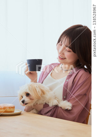 A woman drinking coffee while holding a Maltese dog; a relaxing morning lifestyle with pets. A woman drinking coffee while holding a Maltese dog; a relaxing morning lifestyle with pets. 138528967