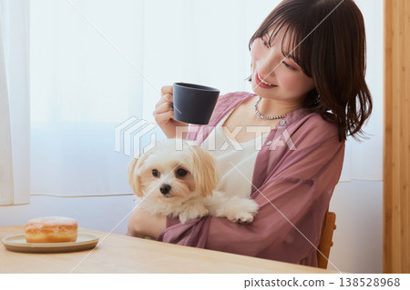 A woman drinking coffee while holding a Maltese dog; a relaxing morning lifestyle with pets. A woman drinking coffee while holding a Maltese dog; a relaxing morning lifestyle with pets. 138528968