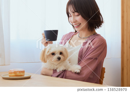 A woman drinking coffee while holding a Maltese dog; a relaxing morning lifestyle with pets. 138528970