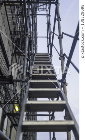 A view looking up at the construction scaffolding and access stairs assembled at the exterior wall construction site. 138529098