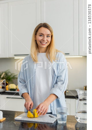 Young woman squeezing lemon into water tumbler in kitchen for fresh vitamin hydration morning habit Young woman squeezing lemon into water tumbler in kitchen for fresh vitamin hydration morning habit 138530378