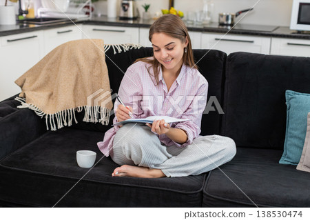 Young woman drinks espresso writes goals in notebook plans week and smiles with calm focused energy Young woman drinks espresso writes goals in notebook plans week and smiles with calm focused energy 138530474