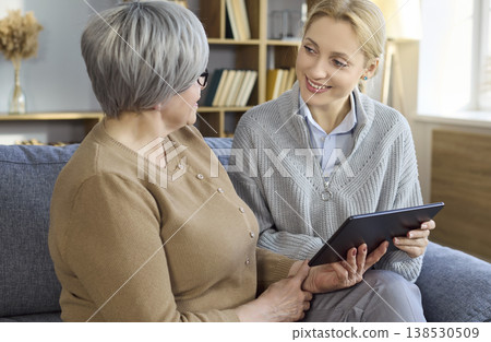 Caregiver supporting senior woman with tablet while chatting together on home sofa Caregiver supporting senior woman with tablet while chatting together on home sofa 138530509