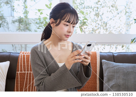 一位女士在客廳看著她的智慧型手機；客廳裡展現著輕鬆的生活方式。 138530510