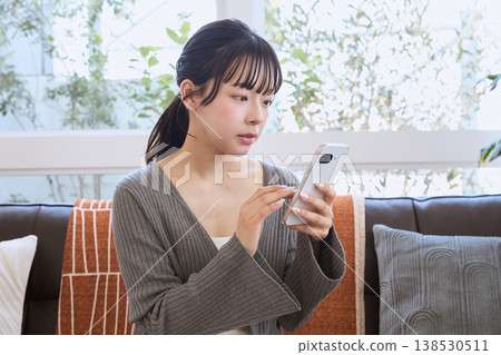 一位女士在客廳看著她的智慧型手機；客廳裡展現著輕鬆的生活方式。 138530511