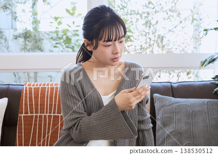 一位女士在客廳看著她的智慧型手機；客廳裡展現著輕鬆的生活方式。 138530512
