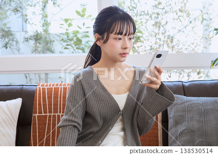 一位女士在客廳看著她的智慧型手機；客廳裡展現著輕鬆的生活方式。 138530514