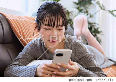一位女士正在客廳裡享受她的智慧型手機;輕鬆愜意的生活方式。 一位女士正在客廳裡享受她的智慧型手機;輕鬆愜意的生活方式。 138530515