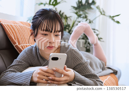 一位女士正在客廳裡享受她的智慧型手機;輕鬆愜意的生活方式。 一位女士正在客廳裡享受她的智慧型手機;輕鬆愜意的生活方式。 138530517