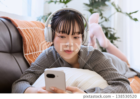 一位女士戴著耳機，在客廳享受智慧型手機帶來的輕鬆生活。 138530520