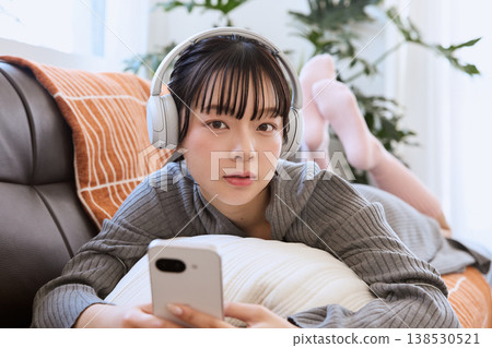 A woman enjoying her smartphone with headphones on; a relaxed lifestyle in the living room. 138530521