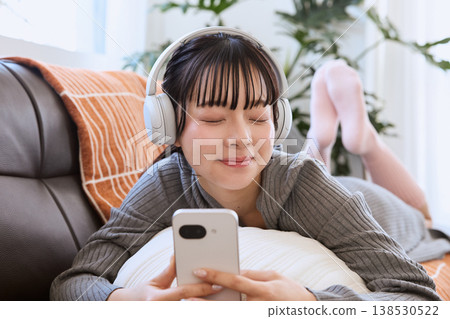 一位女士戴著耳機，在客廳享受智慧型手機帶來的輕鬆生活。 138530522