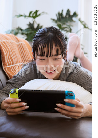 A woman playing a handheld game console; relaxing at home on a holiday. 138530526