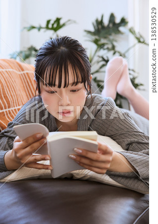 A woman lying on the sofa reading a book; relaxing reading time at home. 138530529