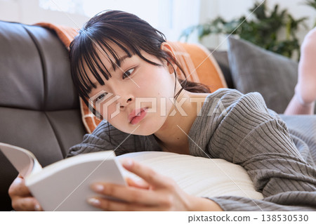 A woman lying on the sofa reading a book; relaxing reading time at home. A woman lying on the sofa reading a book; relaxing reading time at home. 138530530