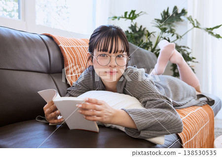 一位戴眼鏡的女士正在看書；在家中享受輕鬆的閱讀時光。 138530535